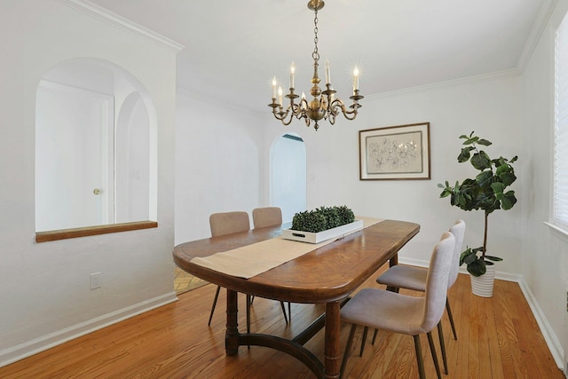 dining space with an inviting chandelier, baseboards, ornamental molding, arched walkways, and wood finished floors
