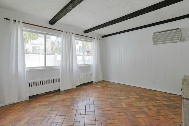 unfurnished room featuring a wall unit AC, a textured ceiling, beam ceiling, radiator heating unit, and brick floor