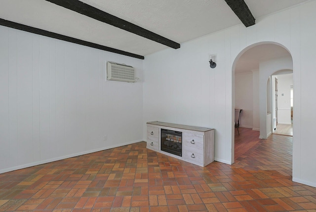 unfurnished room featuring beamed ceiling, baseboards, arched walkways, a wall mounted air conditioner, and brick floor