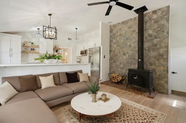living area featuring a wood stove, ceiling fan with notable chandelier, and light wood-style flooring