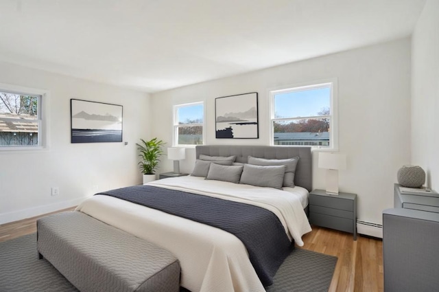 bedroom with light wood finished floors, a baseboard heating unit, and baseboards
