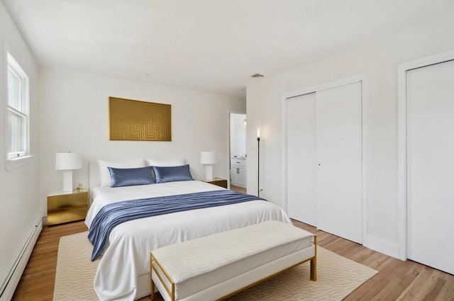 bedroom featuring baseboard heating, visible vents, light wood-style flooring, and multiple closets