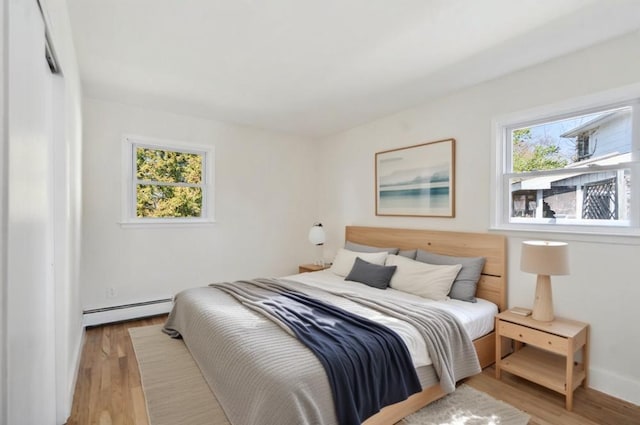 bedroom with light wood finished floors, baseboard heating, and baseboards
