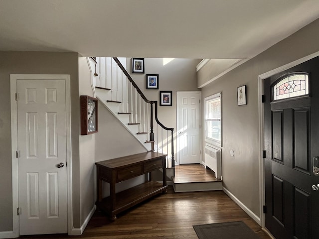 foyer with dark wood finished floors, radiator heating unit, baseboards, and stairway
