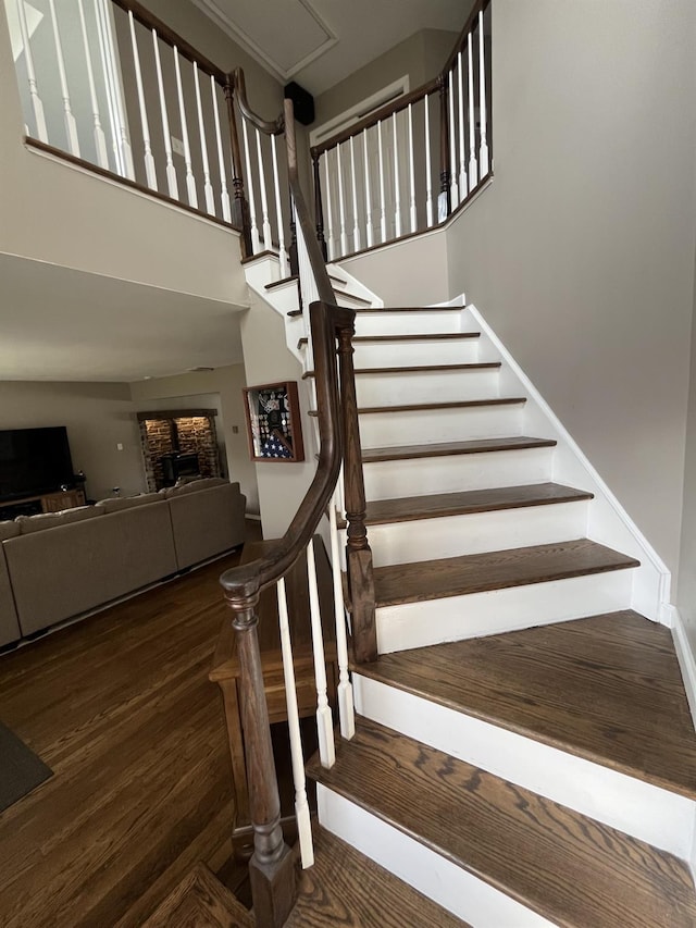 stairs with a towering ceiling, wood finished floors, and a fireplace