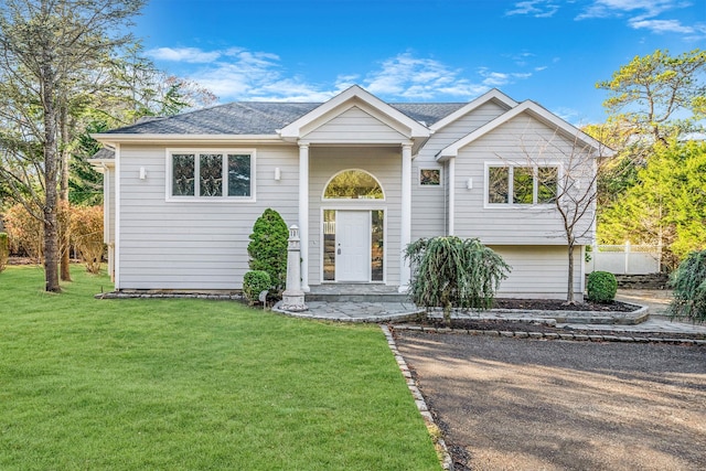 raised ranch featuring a shingled roof and a front yard