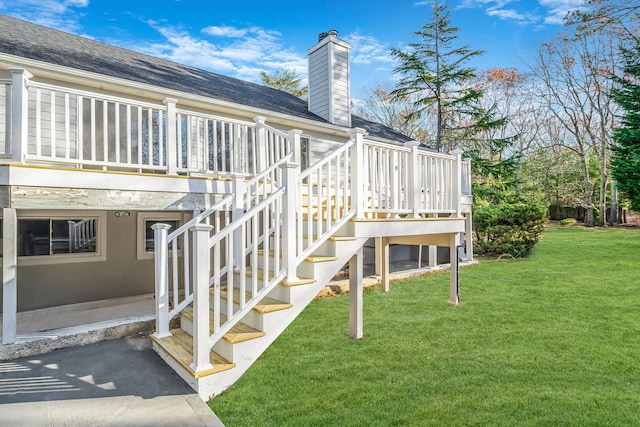 exterior space featuring a lawn, a chimney, a deck, a patio, and roof with shingles