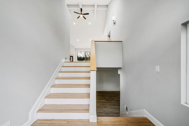 stairs featuring a high ceiling, wood finished floors, beam ceiling, baseboards, and ceiling fan