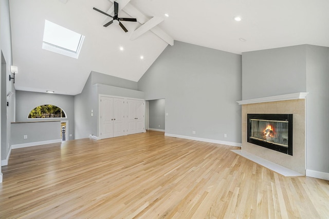 unfurnished living room with wood finished floors, a ceiling fan, beam ceiling, a tiled fireplace, and high vaulted ceiling