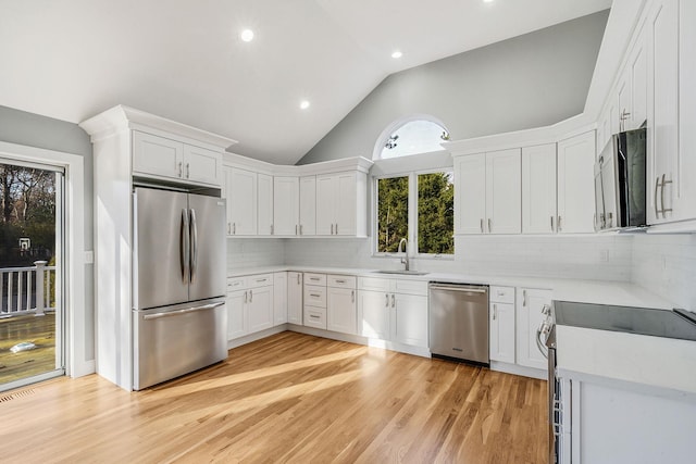 kitchen featuring stainless steel appliances, tasteful backsplash, vaulted ceiling, white cabinetry, and light countertops