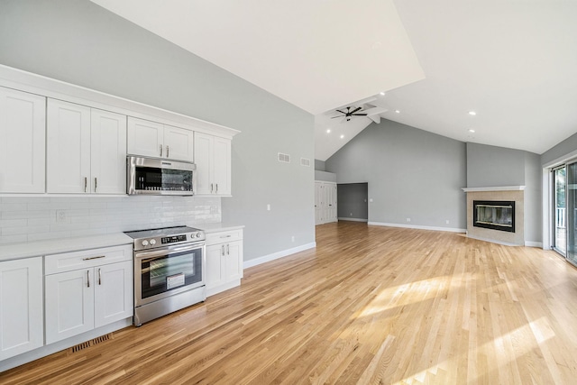 kitchen with stainless steel appliances, light countertops, a glass covered fireplace, tasteful backsplash, and white cabinetry