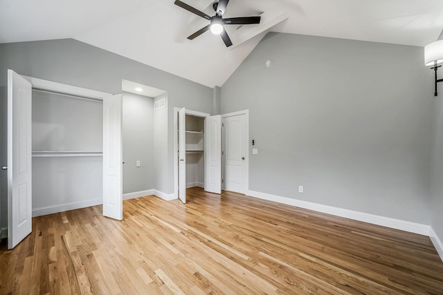 unfurnished bedroom with light wood-type flooring, multiple closets, baseboards, and high vaulted ceiling