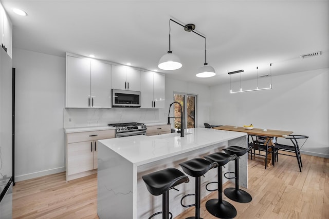 18 Mcbride Pl, Goshen, NY 10924 - kitchen featuring appliances with stainless steel finishes, light wood-style flooring, a breakfast bar, hanging light fixtures, and light stone counters