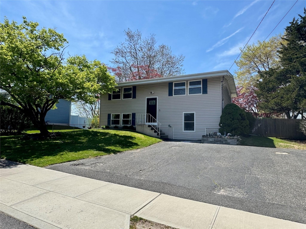 bi-level home featuring driveway, a front yard, and fence