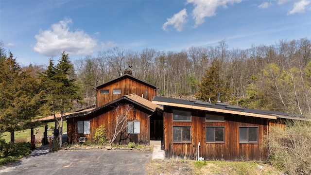 rustic home featuring a chimney, aphalt driveway, and a view of trees