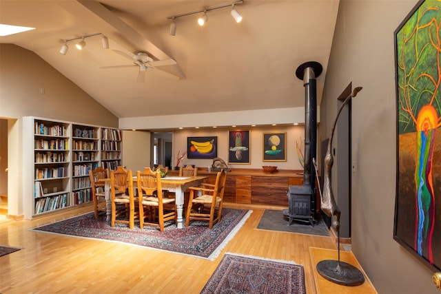 dining space with vaulted ceiling, wood finished floors, rail lighting, and a wood stove