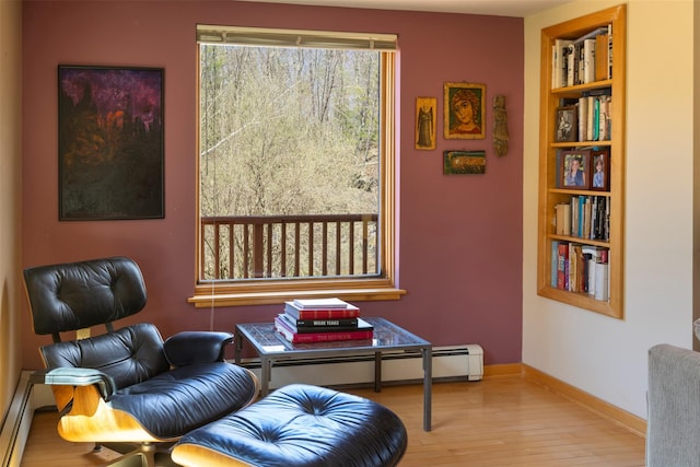 sitting room featuring a baseboard radiator, wood finished floors, built in shelves, and baseboards
