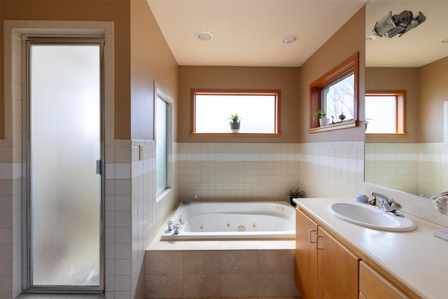 full bath with a stall shower, tile walls, wainscoting, a jetted tub, and vanity