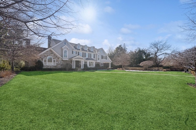 view of front of home with stone siding, a chimney, and a front yard