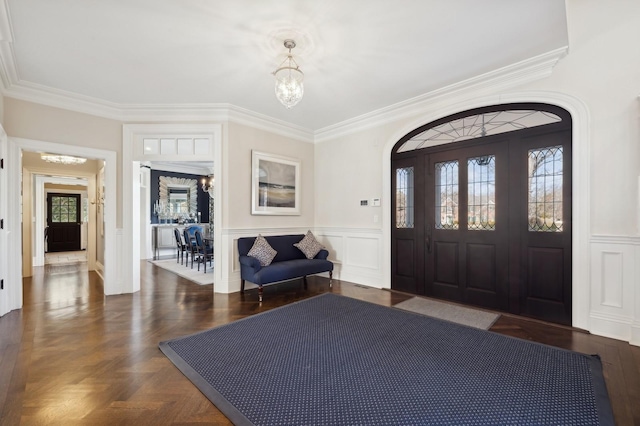 foyer entrance featuring arched walkways, a decorative wall, crown molding, wainscoting, and a notable chandelier