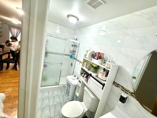bathroom featuring toilet, a stall shower, tile walls, and visible vents