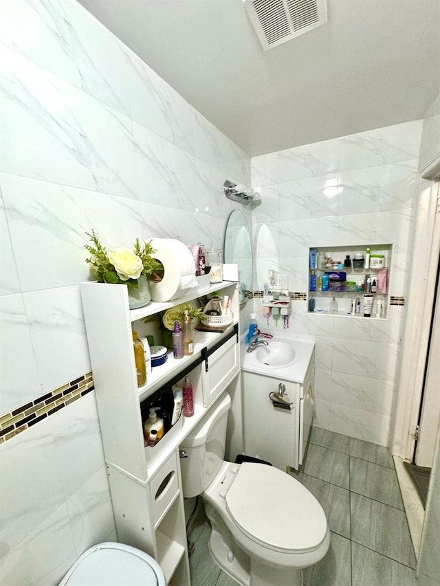bathroom with visible vents, toilet, vanity, and tile walls