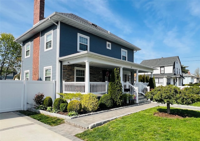 american foursquare style home featuring a chimney, fence, and covered porch