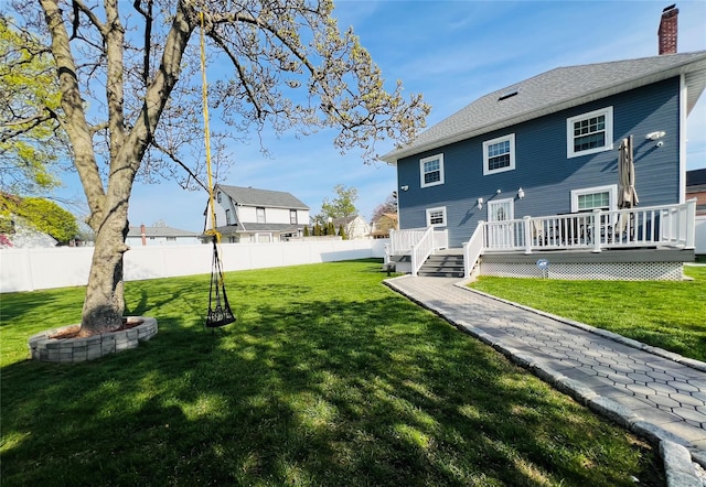 rear view of property featuring a chimney, a wooden deck, fence, and a yard