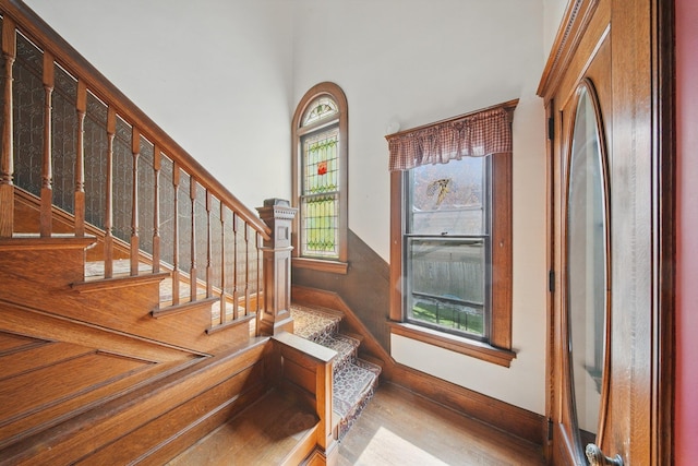 staircase featuring wood finished floors, a towering ceiling, and baseboards