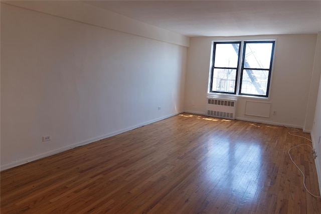 empty room featuring baseboards, wood finished floors, and radiator