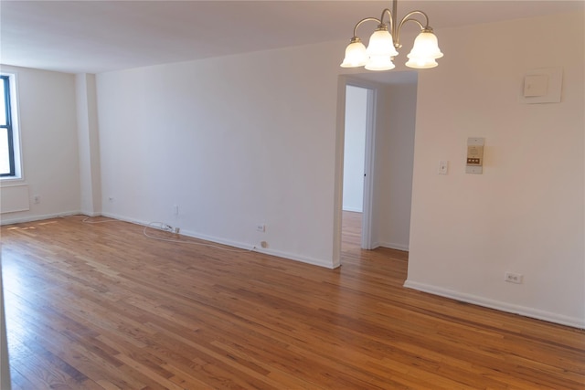 empty room featuring baseboards, a chandelier, and light wood-style floors