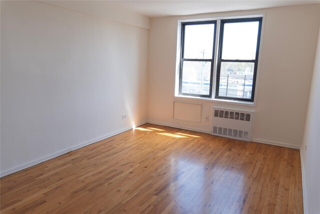 unfurnished room with radiator, light wood-type flooring, and baseboards
