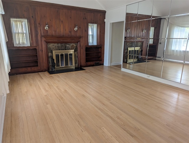 unfurnished living room with baseboards, a stone fireplace, lofted ceiling, and light wood-type flooring