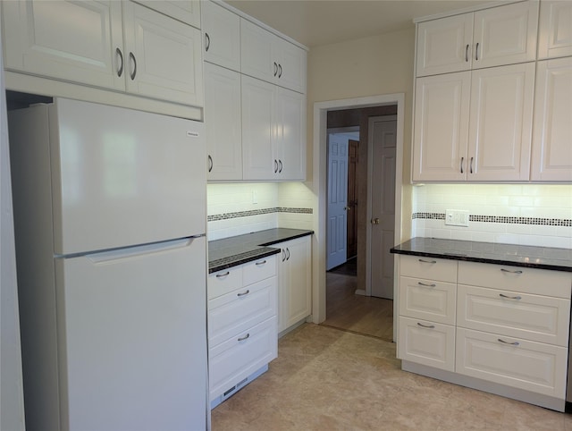 kitchen with freestanding refrigerator, backsplash, white cabinets, and dark stone counters