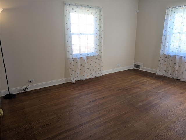 unfurnished room with baseboards, visible vents, and dark wood-type flooring
