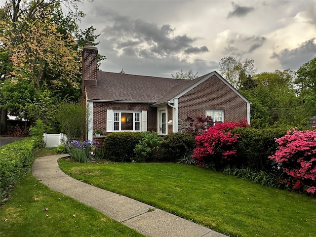 view of front of home with brick siding, a shingled roof, a front yard, and a chimney
