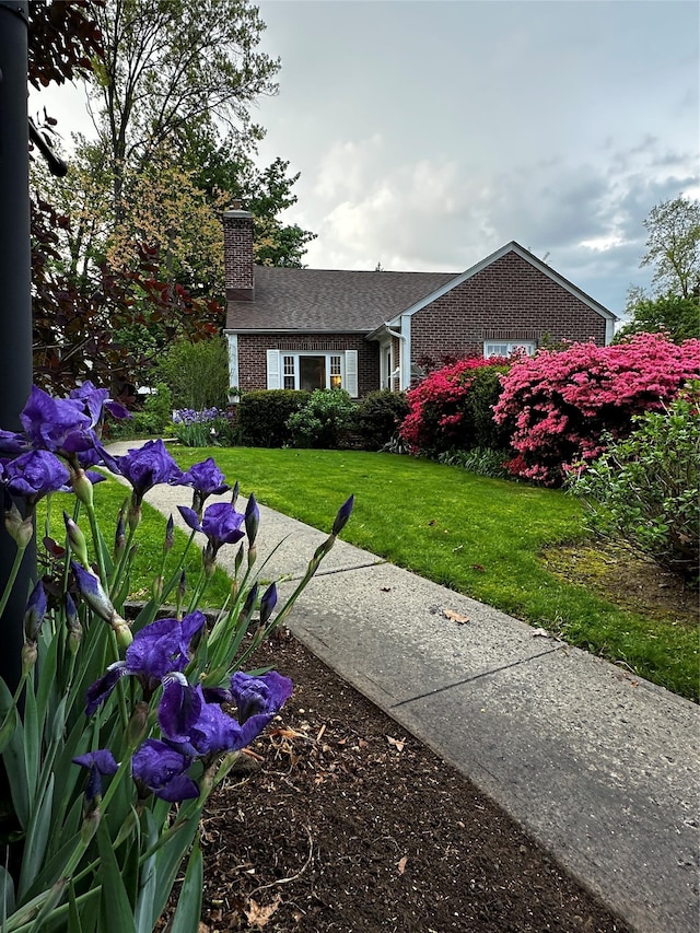 view of front of house with brick siding, a front lawn, and a chimney