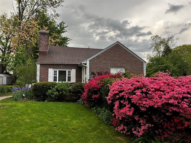 exterior space with a front yard, a shed, a chimney, brick siding, and a shingled roof