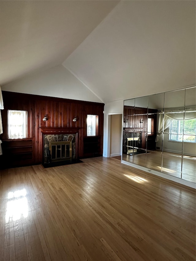 unfurnished living room featuring high vaulted ceiling, a fireplace, wood walls, and wood finished floors