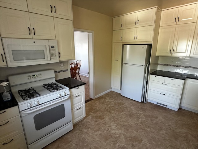 kitchen with dark countertops, white cabinetry, dark floors, and white appliances