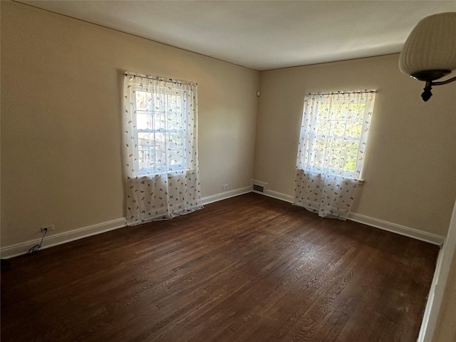 unfurnished room featuring baseboards, visible vents, dark wood-style floors, and a wealth of natural light