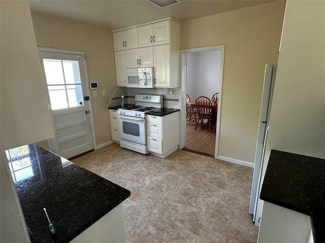 kitchen with dark countertops, white cabinets, baseboards, and white appliances