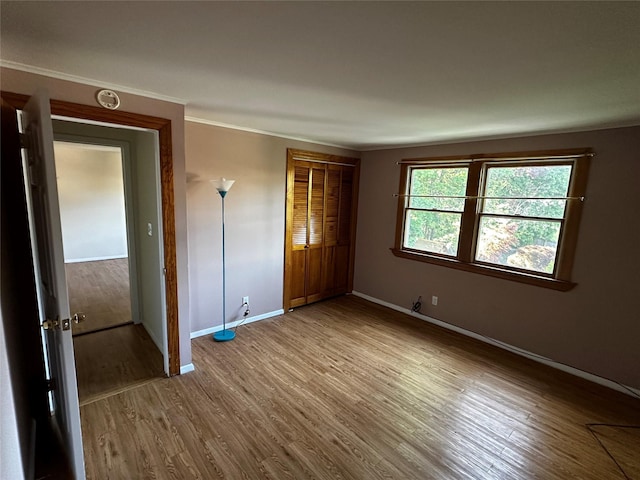 unfurnished bedroom with baseboards, crown molding, wood finished floors, and a closet