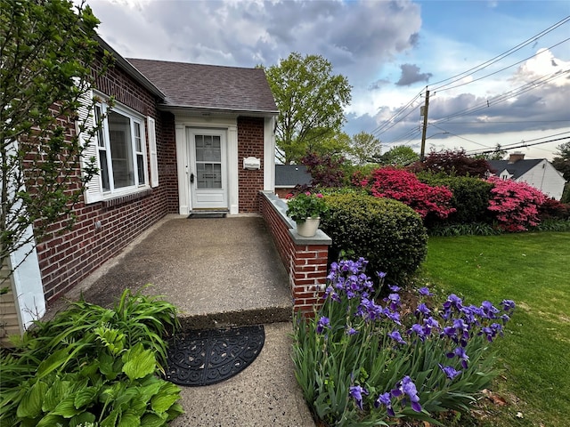 doorway to property with brick siding, roof with shingles, and a yard