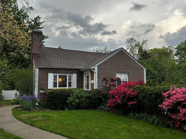 view of front facade featuring roof with shingles, a chimney, a front lawn, and brick siding