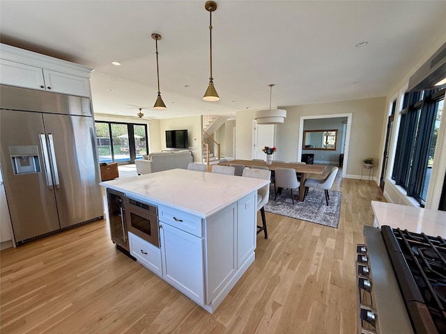 kitchen with hanging light fixtures, light wood finished floors, stainless steel appliances, white cabinetry, and a kitchen bar