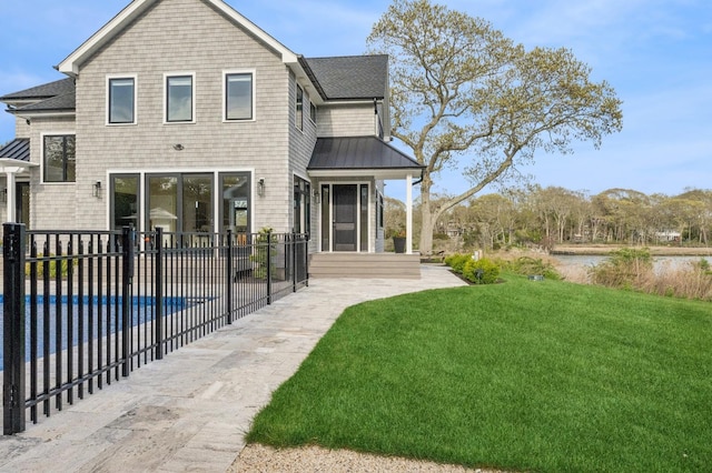 rear view of house featuring a standing seam roof, a lawn, fence, a fenced in pool, and a shingled roof