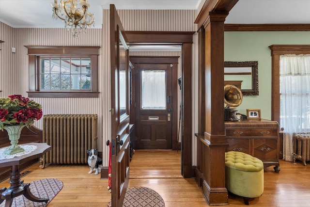 entryway featuring light wood finished floors, radiator heating unit, crown molding, and an inviting chandelier
