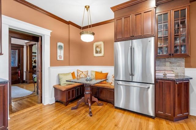 kitchen with crown molding, wainscoting, glass insert cabinets, light wood-type flooring, and stainless steel fridge