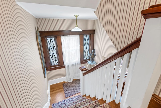 stairway featuring wallpapered walls, wood finished floors, baseboards, and ornamental molding